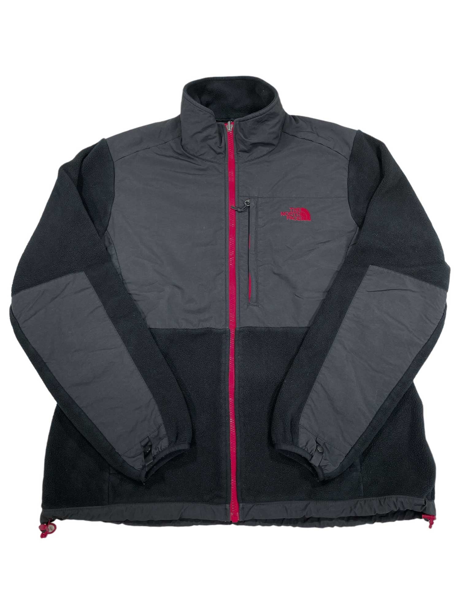 The Denali Jacket is a women's black and dark gray fleece by The North Face, featuring a full front zipper, zippered chest pocket, red left chest logo, adjustable drawcords at hem and sleeves, and made from recycled fleece.