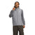 A person smiles, touching their neck, wearing a light gray The North Face Men's Junction Insulated Vest with recycled insulation over a gray long-sleeve shirt and dark olive cargo pants. Both the vest and shirt display The North Face logo.