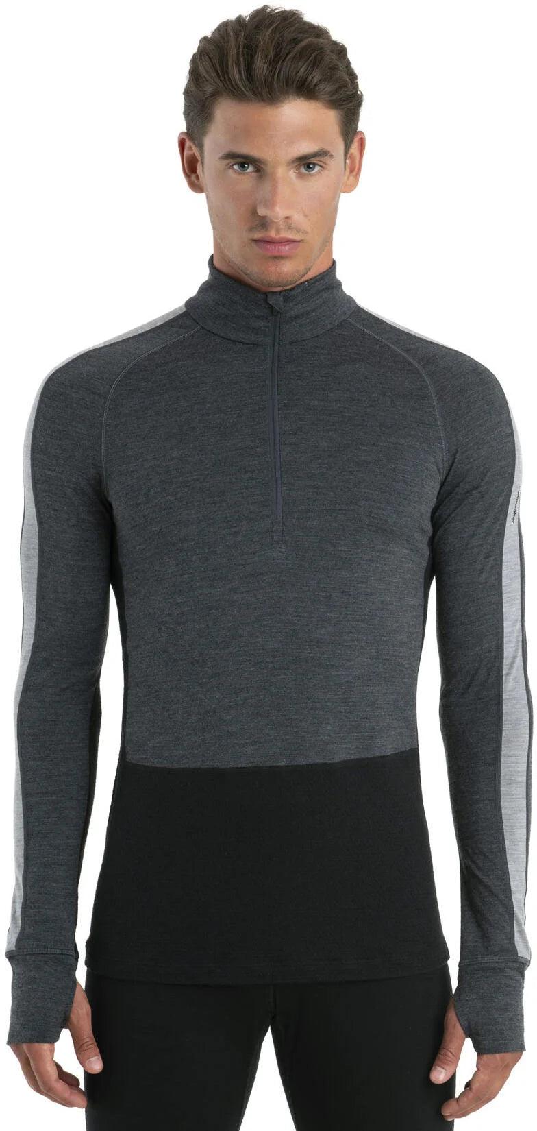 A man with short brown hair wears the Icebreaker Men's Merino 200 Zoneknit LS Half Zip Top in dark gray and black, featuring thumb holes. He stands against a plain white background facing forward with a neutral expression.