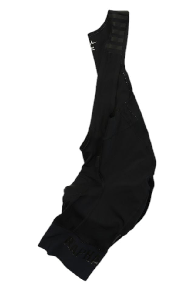 A pair of Rapha Mens Pro Team Bib Shorts II - Regular with shoulder straps is laid flat on a white background, showcasing smooth, stretchy fabric, subtle stitching, a race-grade chamois for comfort, and "Rapha" on the leg cuff.