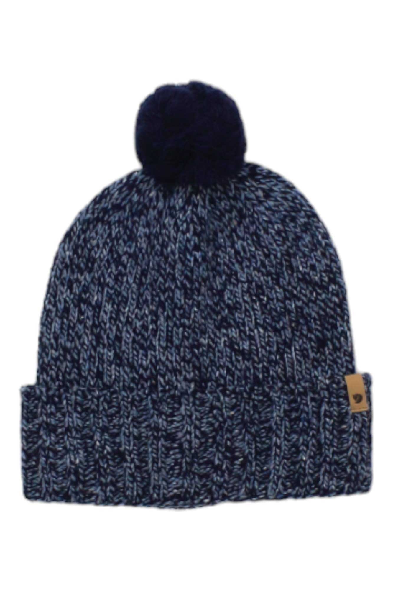 The Fjallraven Ovik Pom Hat features a navy and white marled knit, folded brim, tan logo tag, and dark blue pom-pom—ideal as an outdoor beanie for hiking or winter outings.
