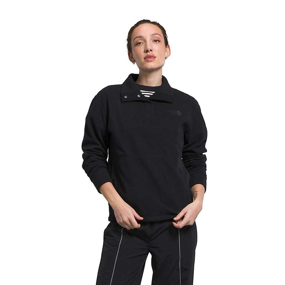 A person wears The North Face Womens Pali Pile Fleece 1/4 Snap in black and matching black pants, both made from recycled polyester, standing against a white background with one hand in their pocket and the other by their side.