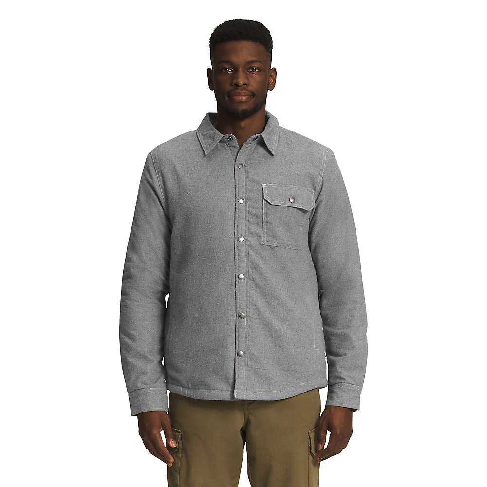 A man stands facing forward, wearing The North Face Mens Campshire Shirt in gray with long sleeves and a chest pocket, paired with khaki pants against a plain white background.