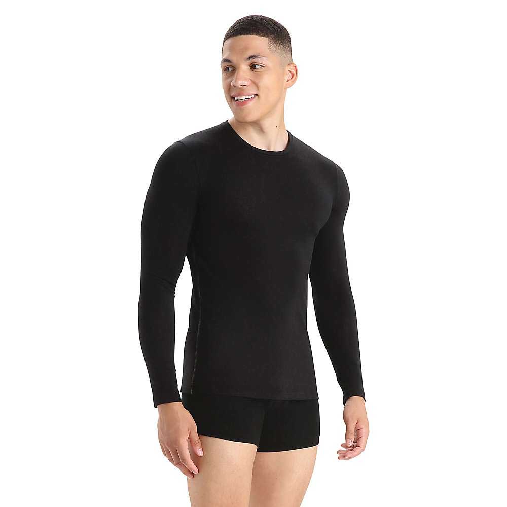 A man in the Icebreaker Mens Anatomica LS Crewe, a fitted black long sleeve shirt, and black boxer briefs stands against a white background, smiling and looking to the side.