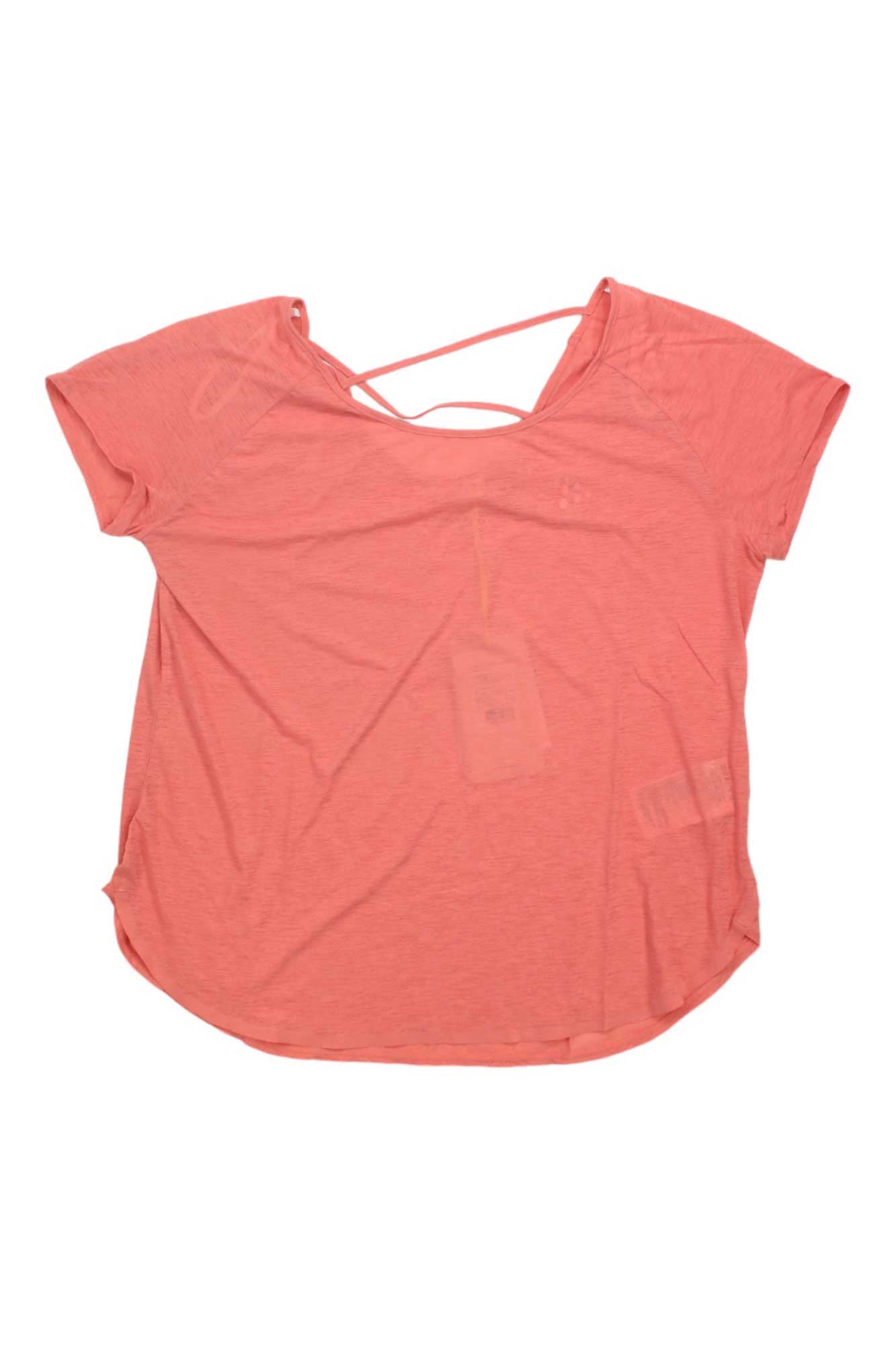 The Craft Sportswear Womens Core Charge Cross Back Tee is a coral pink, short-sleeve, loose-fitting training top with a scoop neckline and crisscross back straps, shown flat on a white background with tags attached.