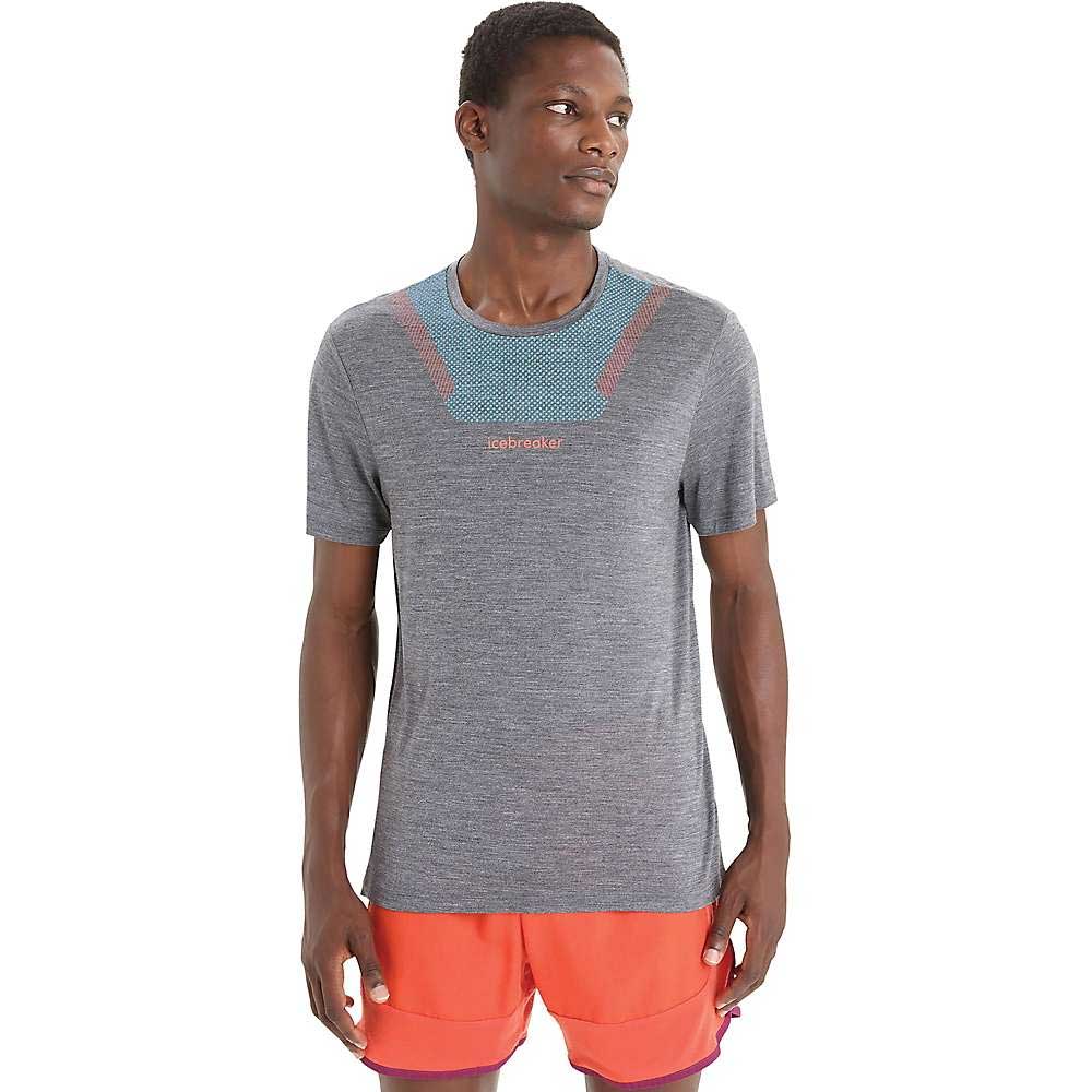 A man faces slightly to the side, wearing the Icebreaker Men's Sphere II SS Tee in grey with blue and red accents and orange shorts, looking off to the right against a plain white background.