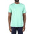 A man in a light green Moosejaw Mens Lager SS Tee with white "MOOSTAR" on the left chest, paired with dark blue jeans, stands against a white background.
