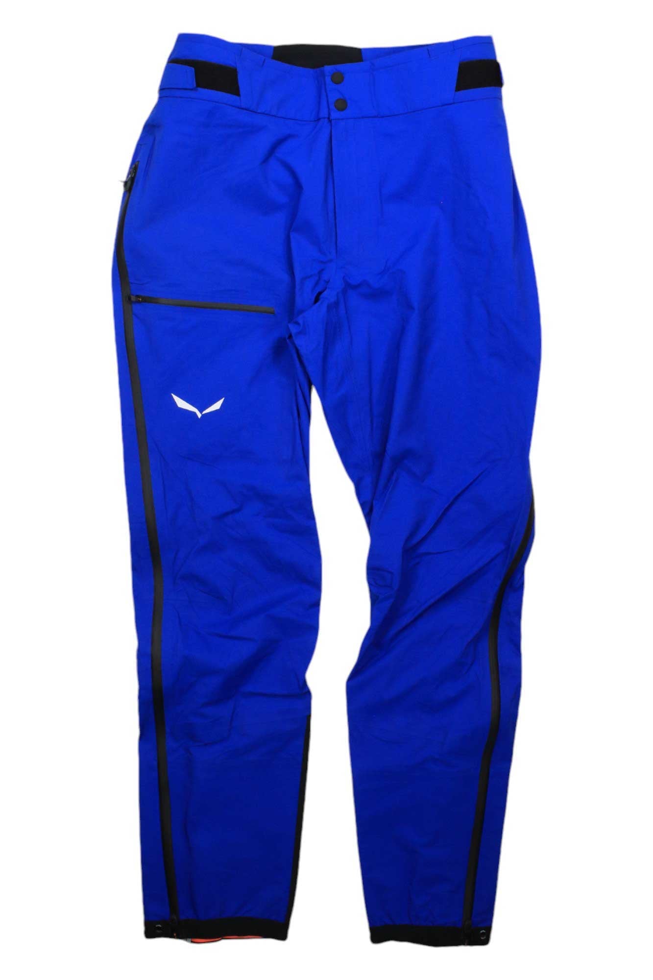 The Salewa Mens Ortles PTX 3L Pant features bright blue, breathable fabric, black adjustable waist tabs, a button closure, a right thigh zipper pocket, black side zippers on both legs, and a small white logo on the right leg.