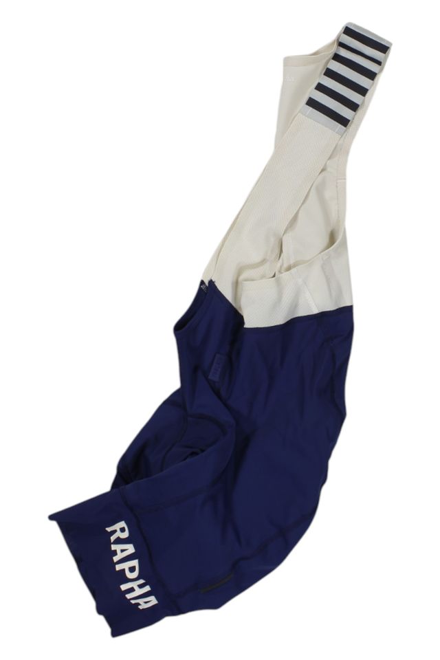 The Rapha Mens Pro Team Bib Shorts II - Regular in blue and white feature a striped strap, race-grade chamois for comfort, and RAPHA printed in white on the left leg cuff.