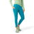A person stands with one hand in a pocket, wearing a light green long-sleeve top, Smartwool Women's Active 7/8 Legging in bright turquoise with moisture-wicking pockets, and gray-green athletic shoes against a plain white background.