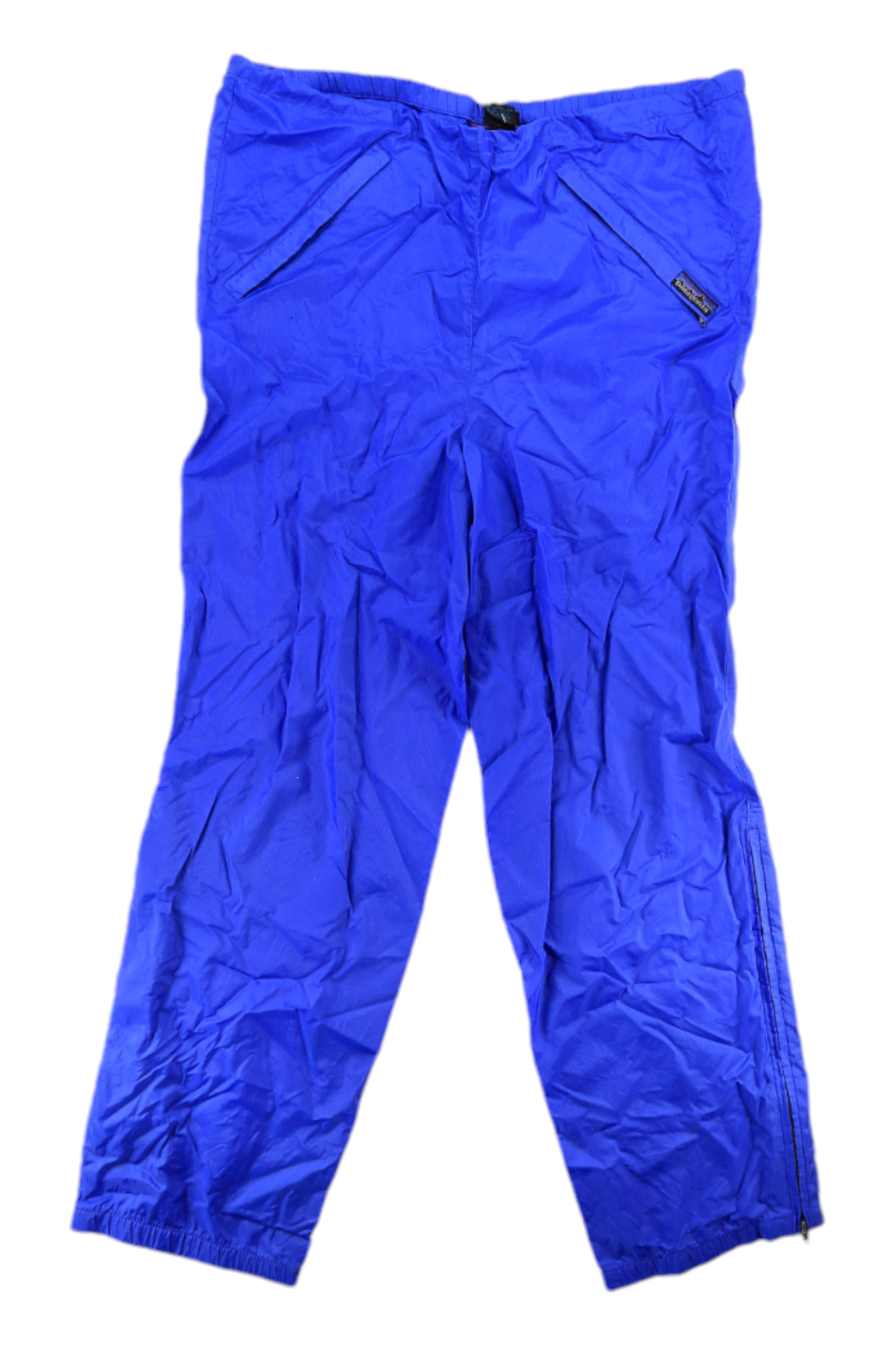Patagonia Mens Vintage Shell Pants in bright blue, featuring a lightweight design, elastic waistband, zippered side pockets, leg zippers for weather protection, and a small logo patch by one pocket. The pants show some wrinkling.