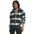 A person wears The North Face Womens Campshire Fleece Hoodie in blue, white, and olive green zigzag pattern, paired with dark green pants and a white undershirt, standing with hands at their sides and looking forward.