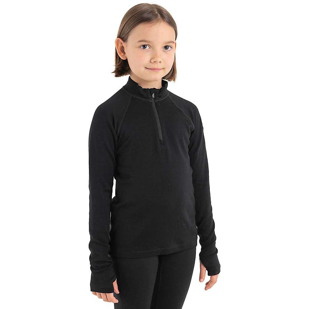 A young child with short brown hair wears an Icebreaker Kids 260 Tech LS Half Zip Top in black and matching pants, standing against a plain white background, looking slightly to the side and smiling softly.