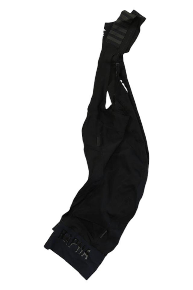 A pair of black Rapha Mens Pro Team Bib Shorts II - Long with shoulder straps and a logo near the cuff, featuring a dual-density chamois pad, laid flat on a white background.