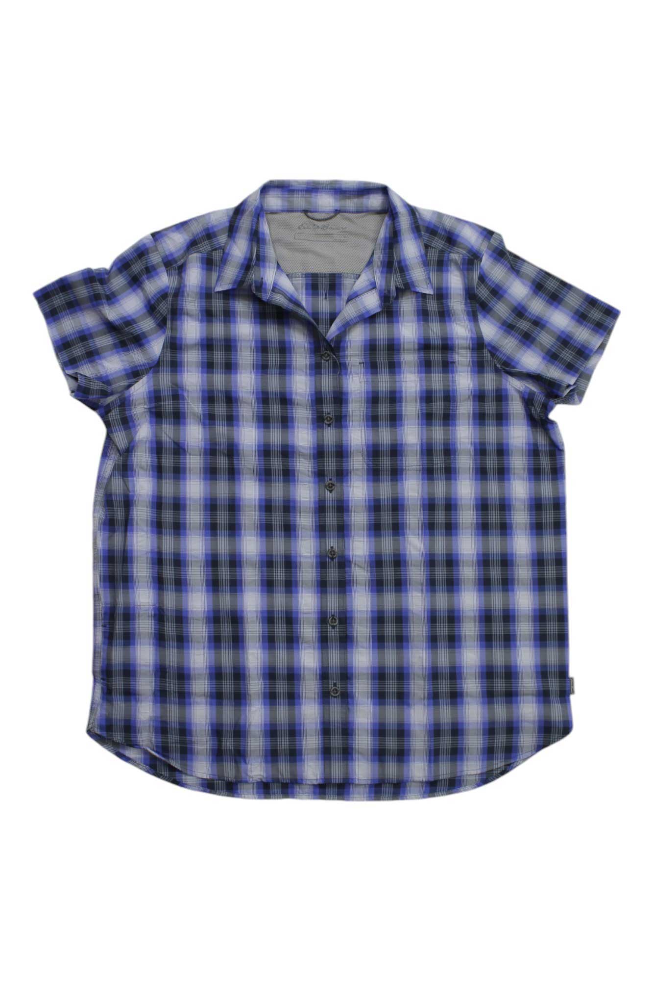 The Eddie Bauer Travex Women’s Mountain 2.0 SS Shirt is a short-sleeve, blue, black, and white plaid button-up with moisture-wicking fabric for comfort, shown laid flat on a white background.