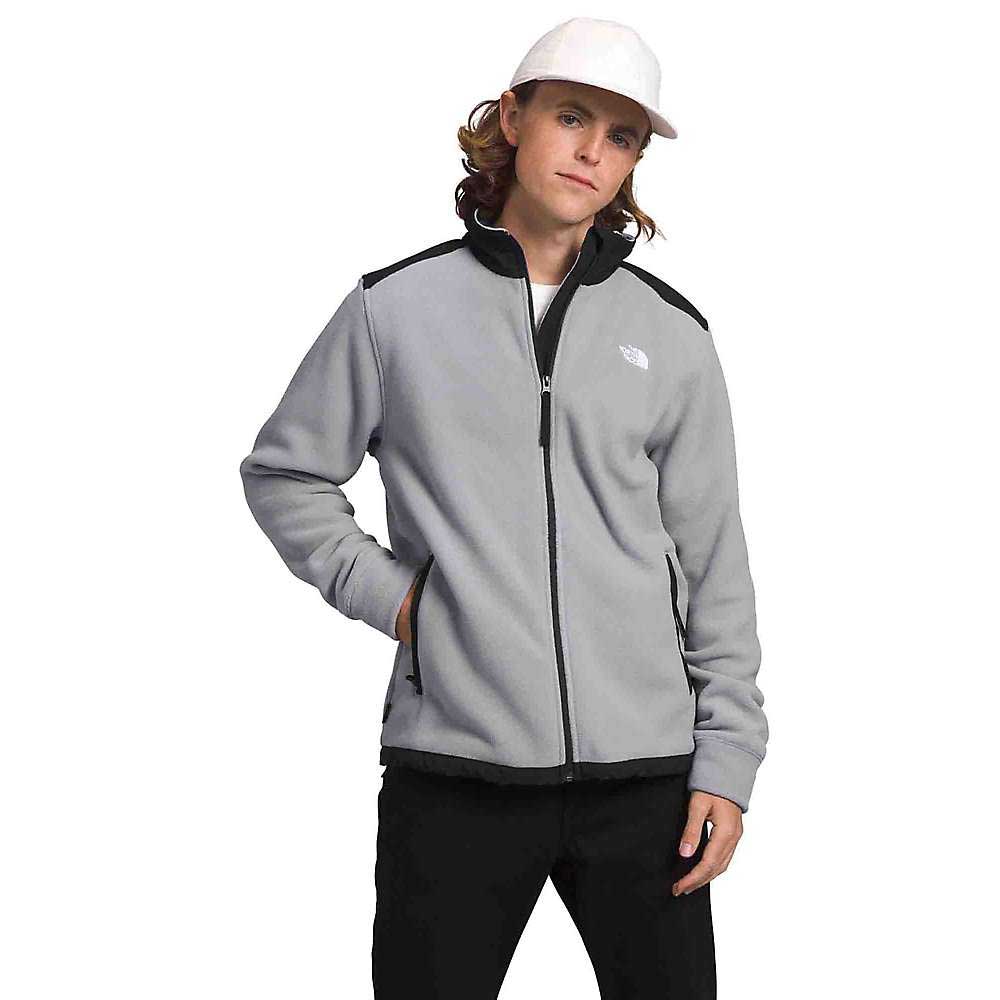 A person wearing The North Face Men's Alpine Polartec 200 Full Zip Jacket in light gray with black trim, paired with black pants and a white cap, stands against a plain white background.