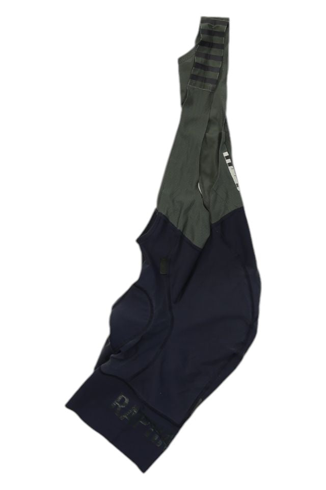 The Rapha Mens Pro Team Bib Shorts II - Regular in navy blue and olive green features wide shoulder straps and a race-grade chamois, inspired by the original Pro Team Bib Shorts, displayed on a white background.