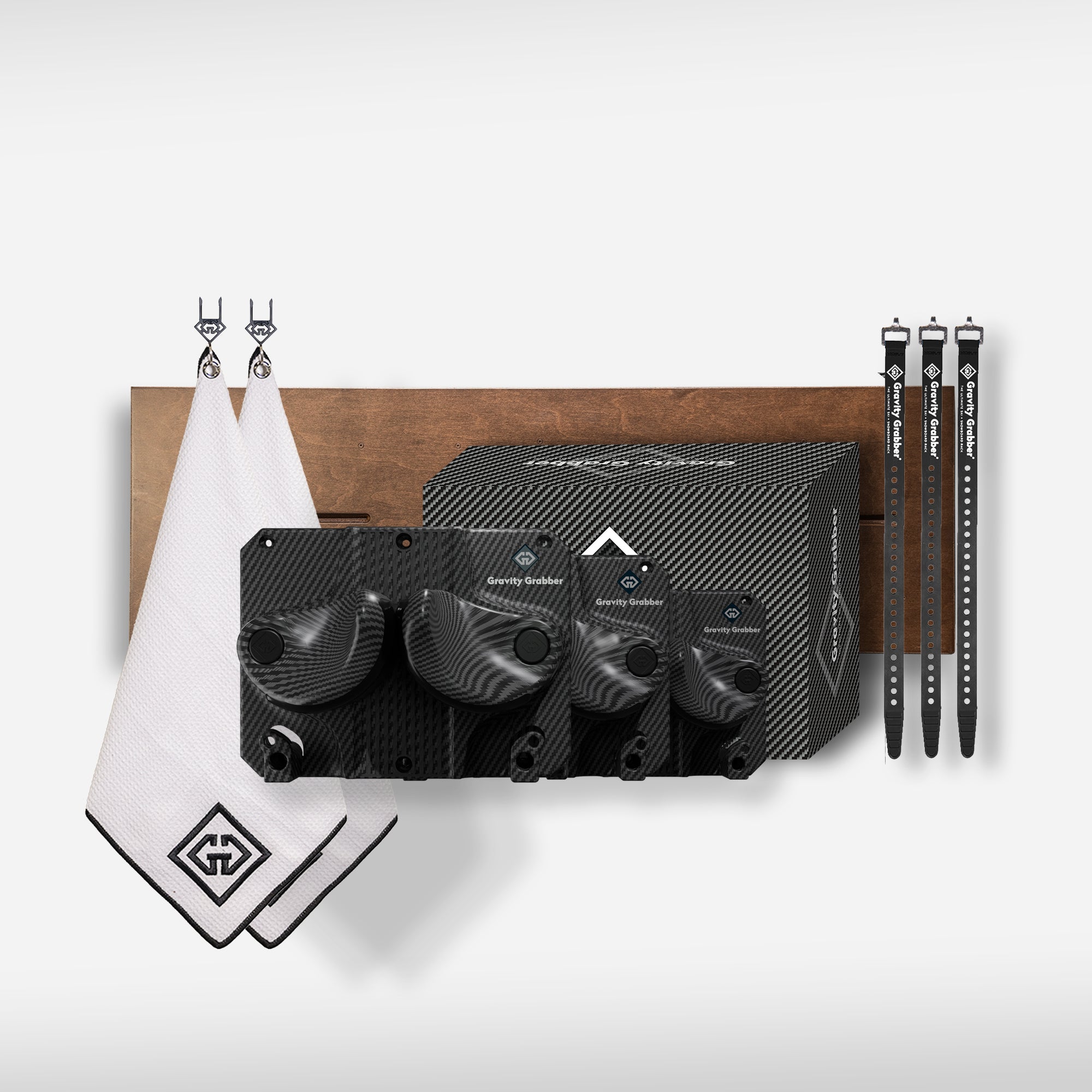 The Carbon Bundle Maple Board includes four carbon fiber-patterned packing cubes, two white towels with black trim, and three black luggage straps—perfect for organizing gear on a wooden shelf in your garage or by your ski and snowboard rack.