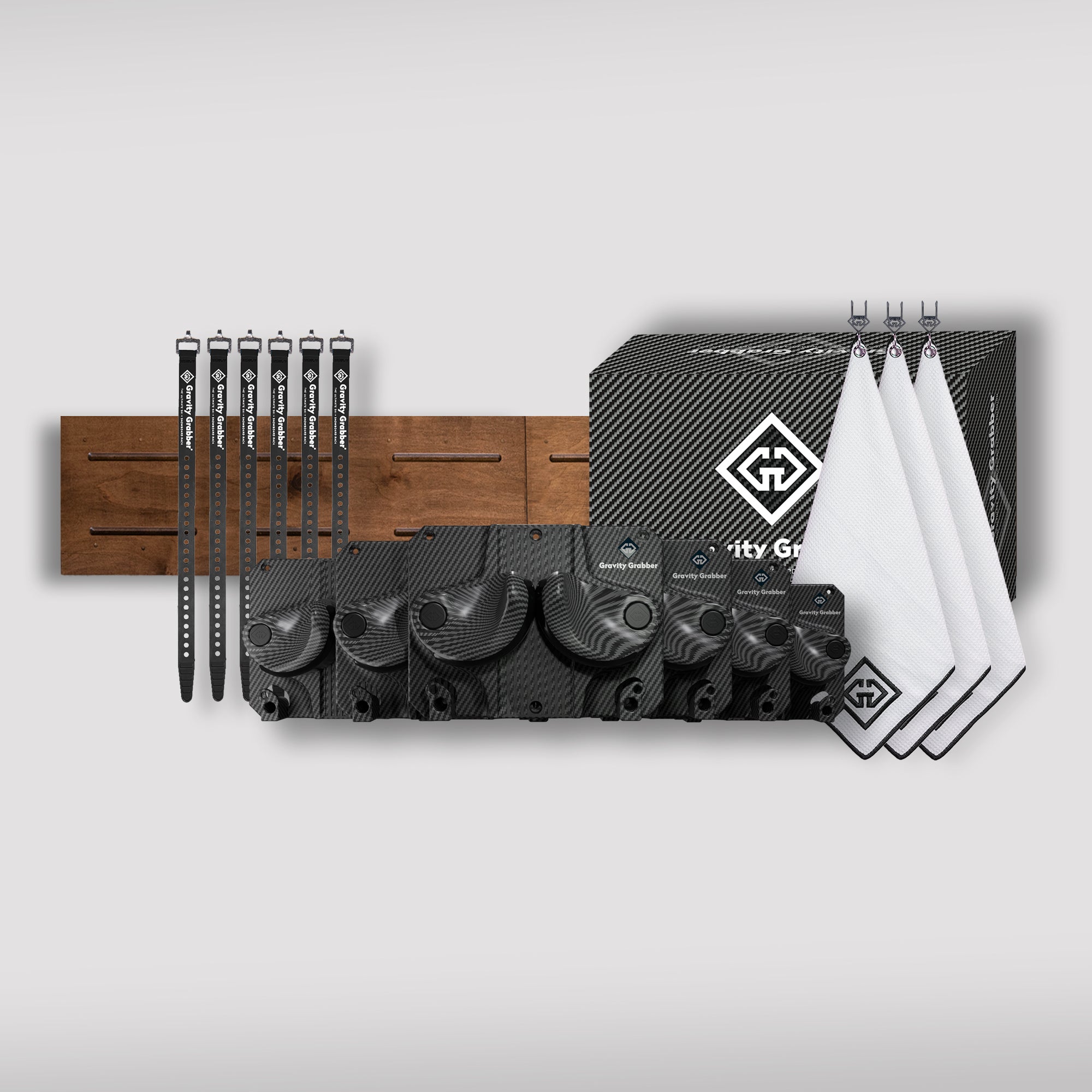 The Carbon Bundle Maple Board kit features black straps, two wooden panels, a black-patterned box, four logoed white cloths, and black components—ideal as a ski and snowboard rack—shown on a light gray background.