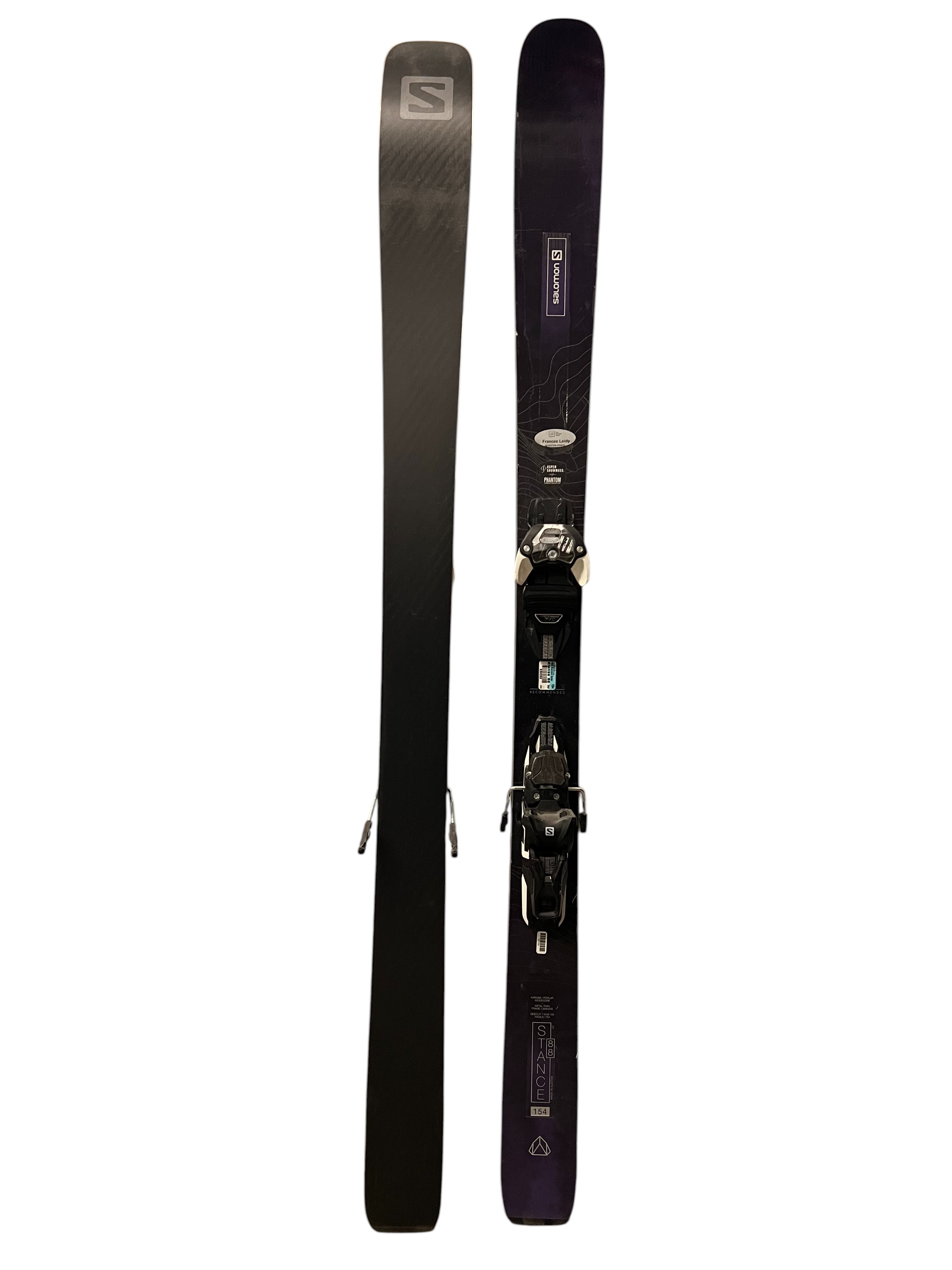 A pair of Salomon Womens Stance 88 Skis with Salomon Warden 11 Bindings—one showing a black base, the other the top with a black and purple design plus attached bindings—are displayed side by side.