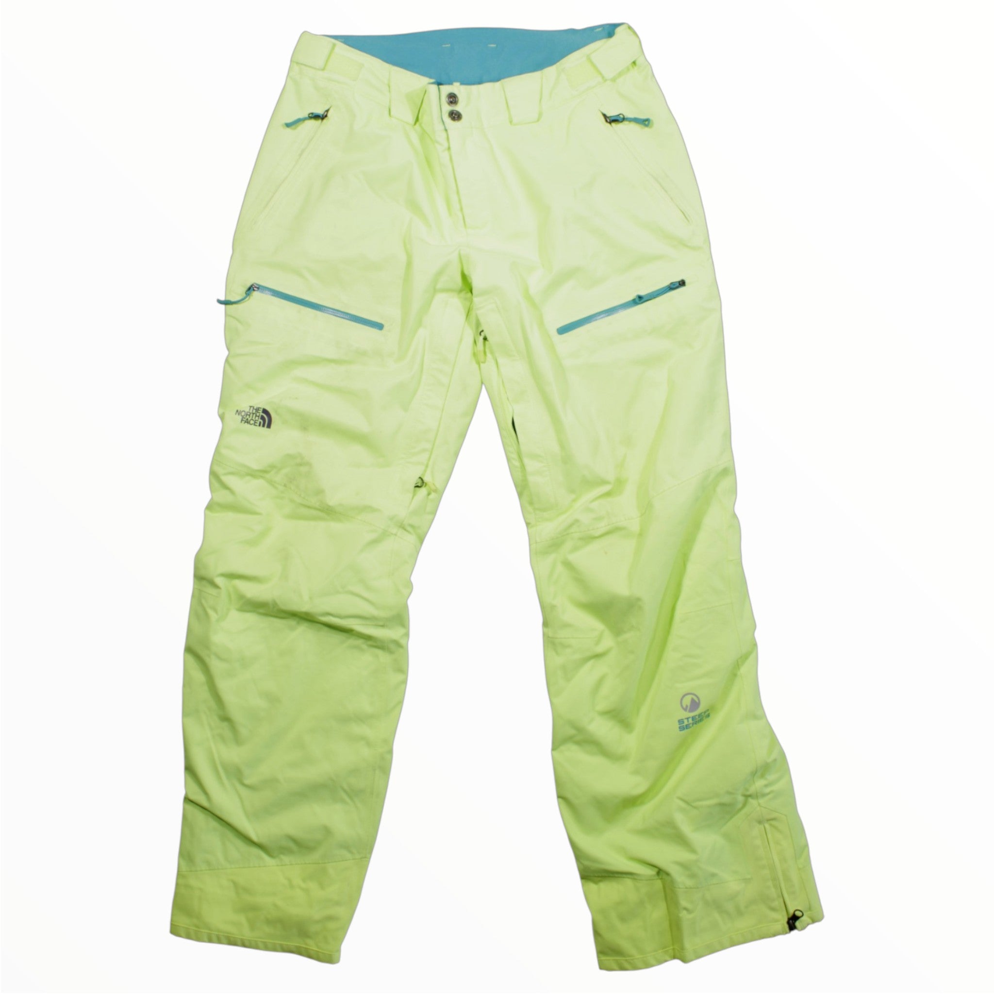 The North Face Womens Steep Series Snow Pants in light green feature multiple zippered pockets, button and zip closure, HyVent Alpha logo on the leg, and a blue inner waistband—designed for alpine movement.