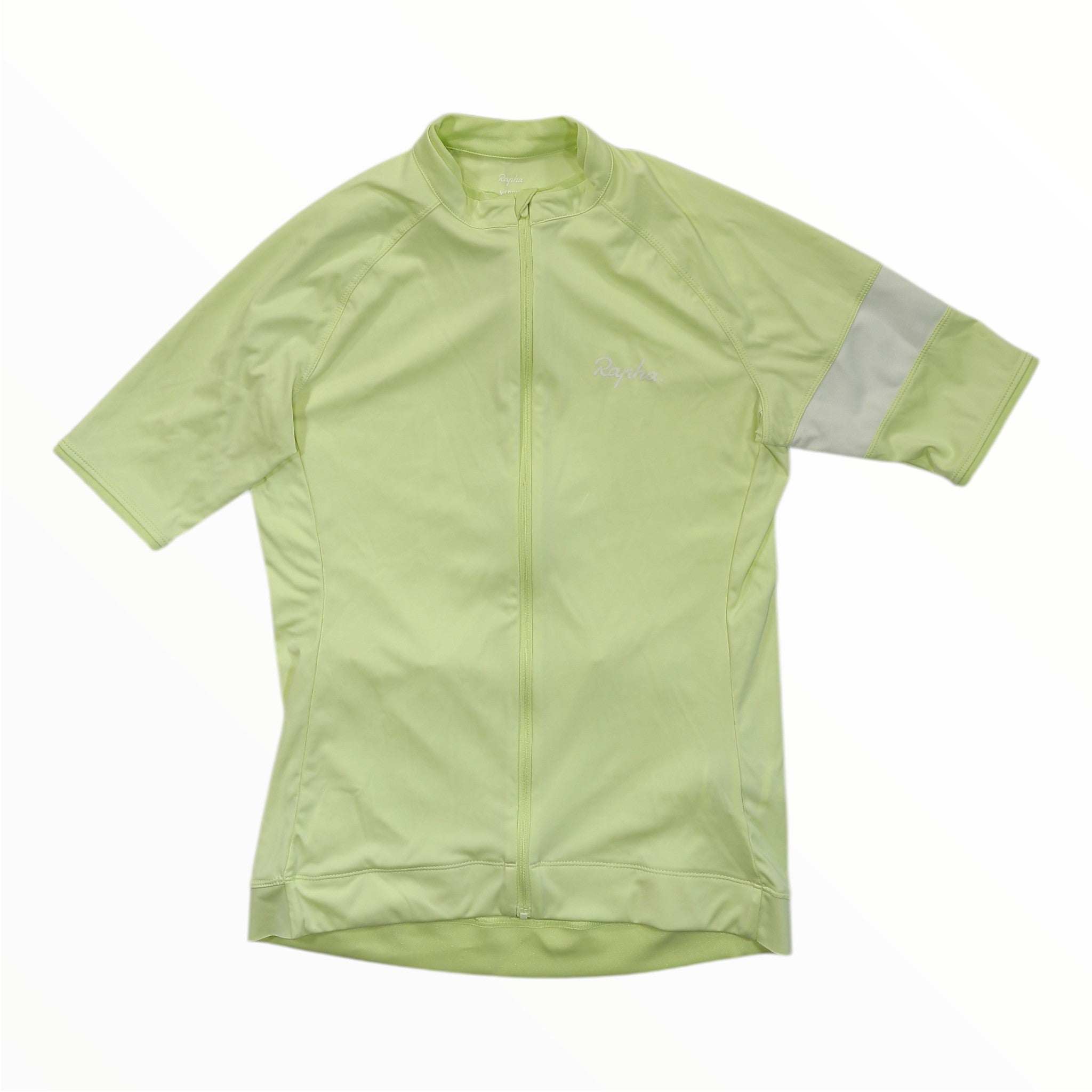 Laid flat on a white background, the Rapha Mens Core Jersey features a light green color, short sleeves, a full front zipper, and a subtle logo on the chest. A reflective strip accents the right sleeve, highlighting Rapha’s commitment to quality and style in men’s cycling apparel.