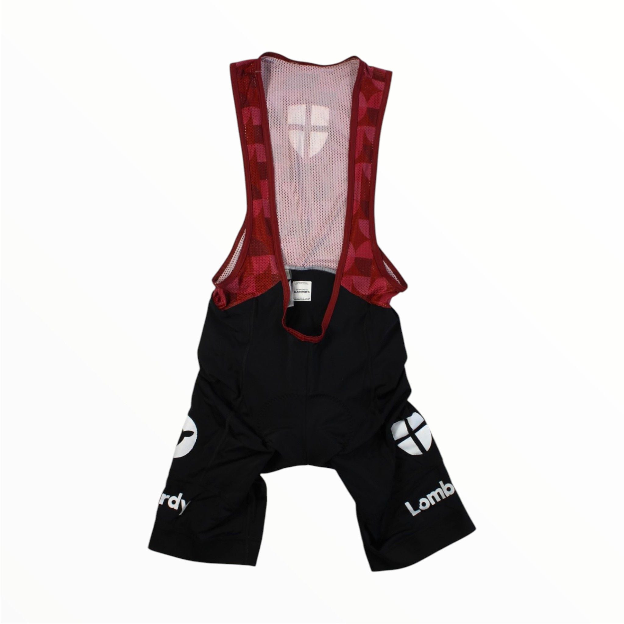 The Black Sheep Cycling Mens Lombardy Bib Shorts feature white logos and "Lombardy" text on black fabric, red mesh suspenders with a geometric pattern, and a white cross symbol on the chest for high-performance cycling.