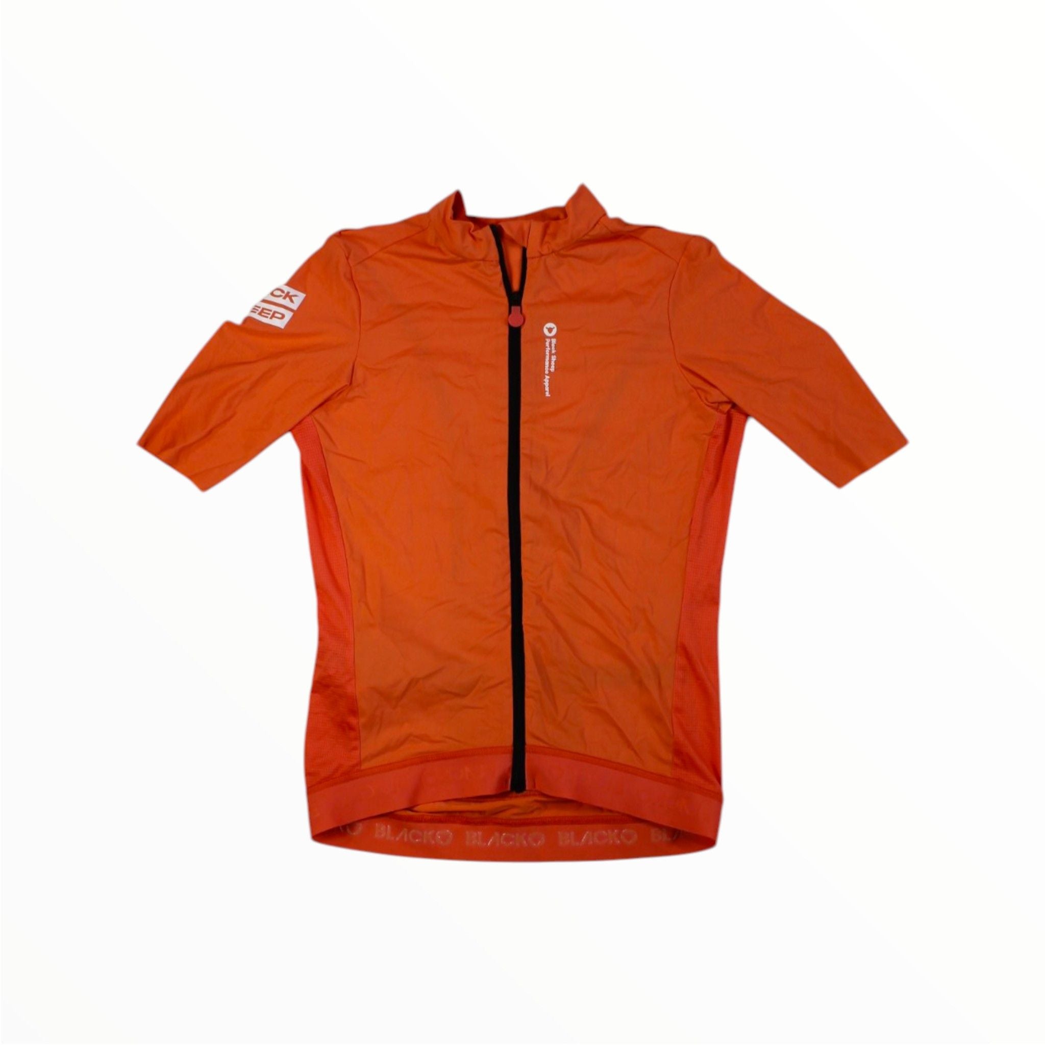 The Black Sheep Cycling Mens Team SS Jersey is an orange men's cycling top with a full-length black zipper, small white chest logo, and a white text patch on the left sleeve. Moisture-wicking fabric. Shown on a white background.