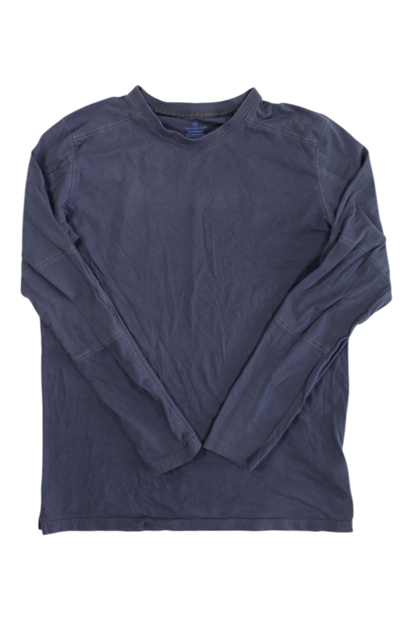 The Kuhl Mens Bravado Long Sleeve is a navy blue crew neck shirt made from Wildfibre organic cotton, shown laid flat with visible seam stitching and slight wrinkles on a white background.
