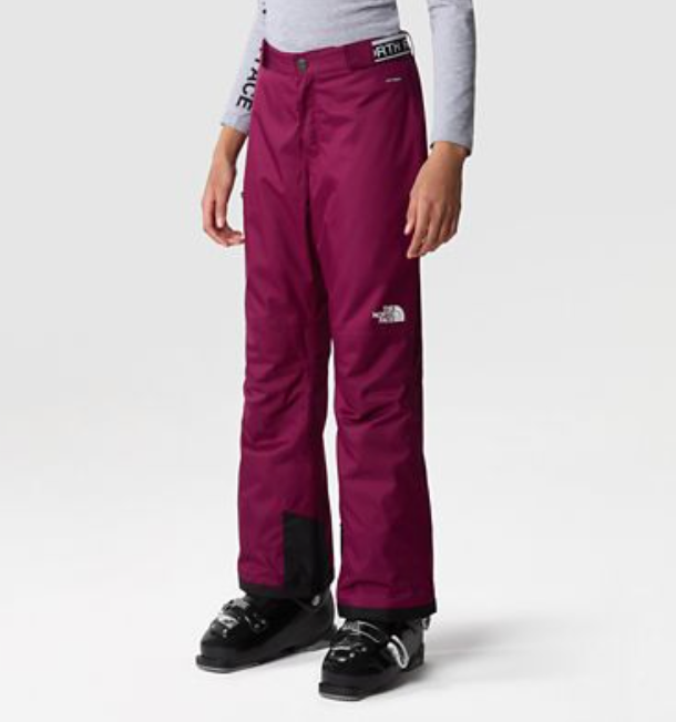 A child models The North Face Girls Freedom Insulated Pant in magenta with a light gray long-sleeve top and black ski boots, standing confidently against a plain light gray background. Ideal insulated snow pants for girls' winter adventures.
