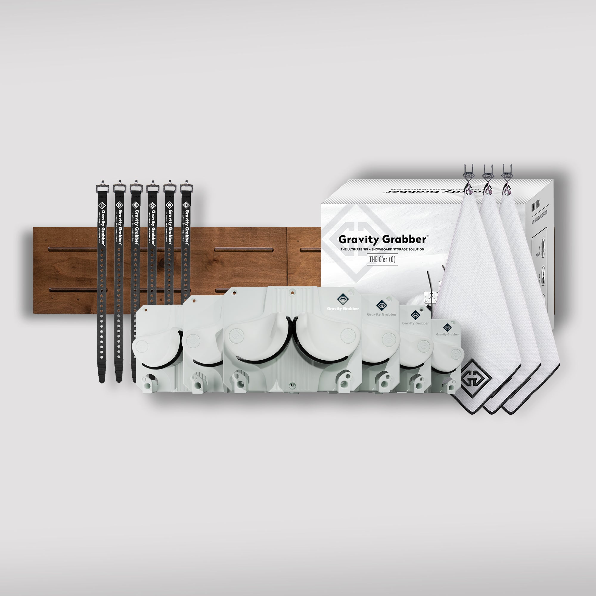 The White Bundle Maple Board garage storage kit includes a wooden wall mount, four black straps, four white hooks, a Gravity Grabber box, four foldable Gravity Grabbers, and three white towels with black square logos on a light gray background.