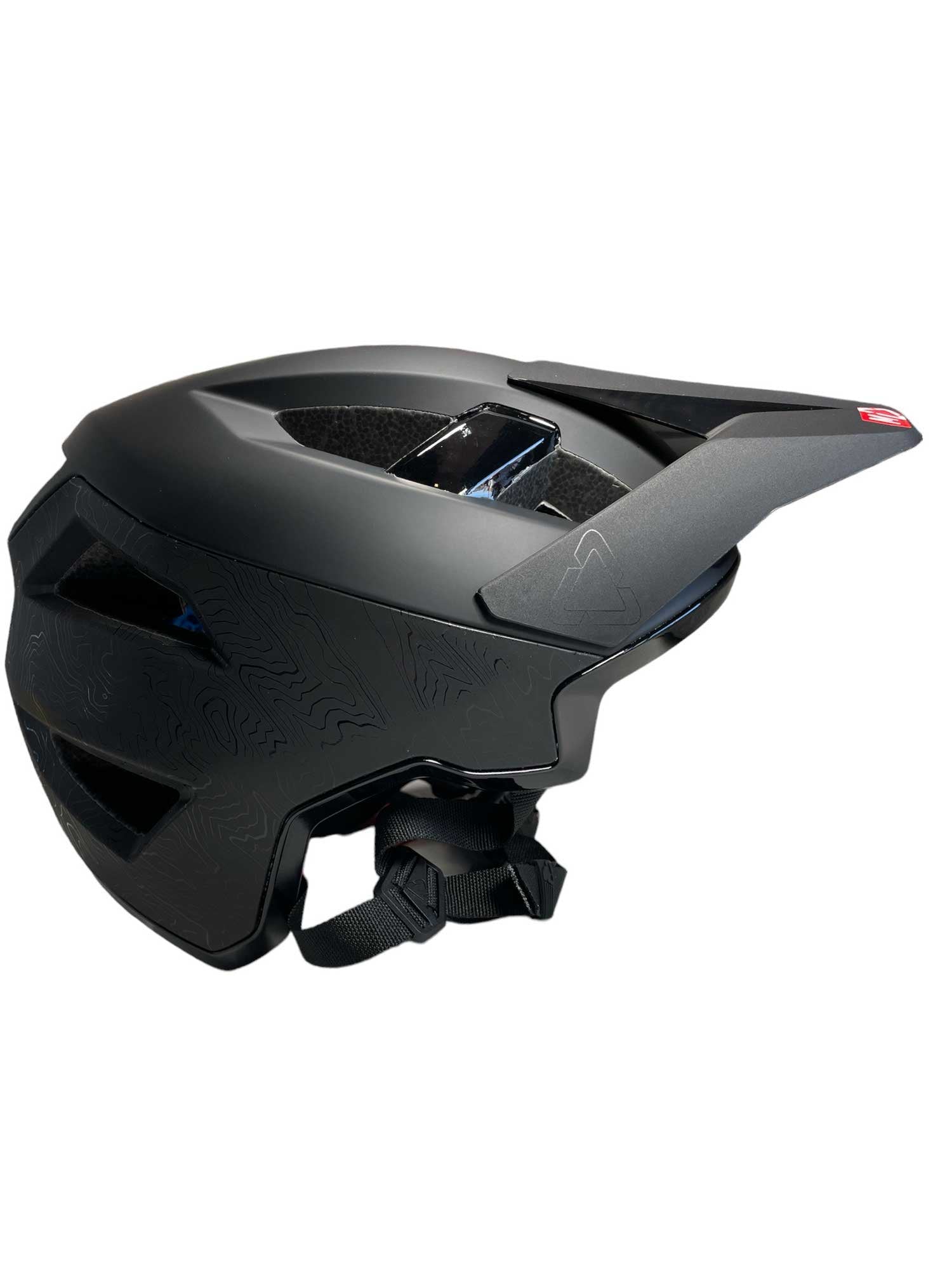 The Leatt MTB All Mountain 3.0 V23 Helmet is a lightweight matte black mountain bike helmet with an extended visor, ventilation holes, and adjustable chin strap, shown from the side against a white background for comfort and style on every ride.