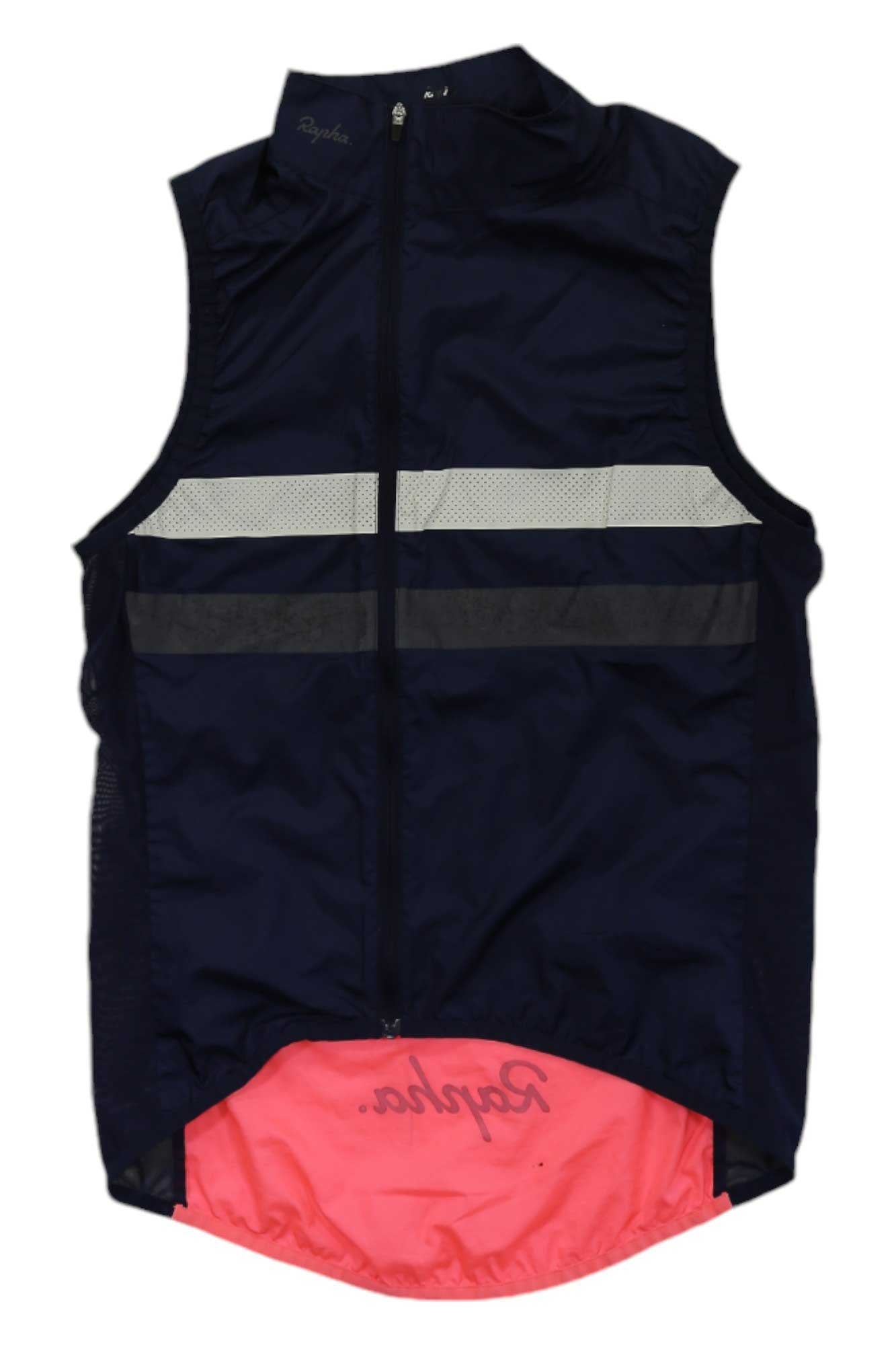 The Rapha Mens Brevet Gilet is a breathable, sleeveless cycling vest in navy blue with reflective stripes, a pink lower back featuring the Rapha logo, front zipper, and high collar for comfort and visibility on every ride.