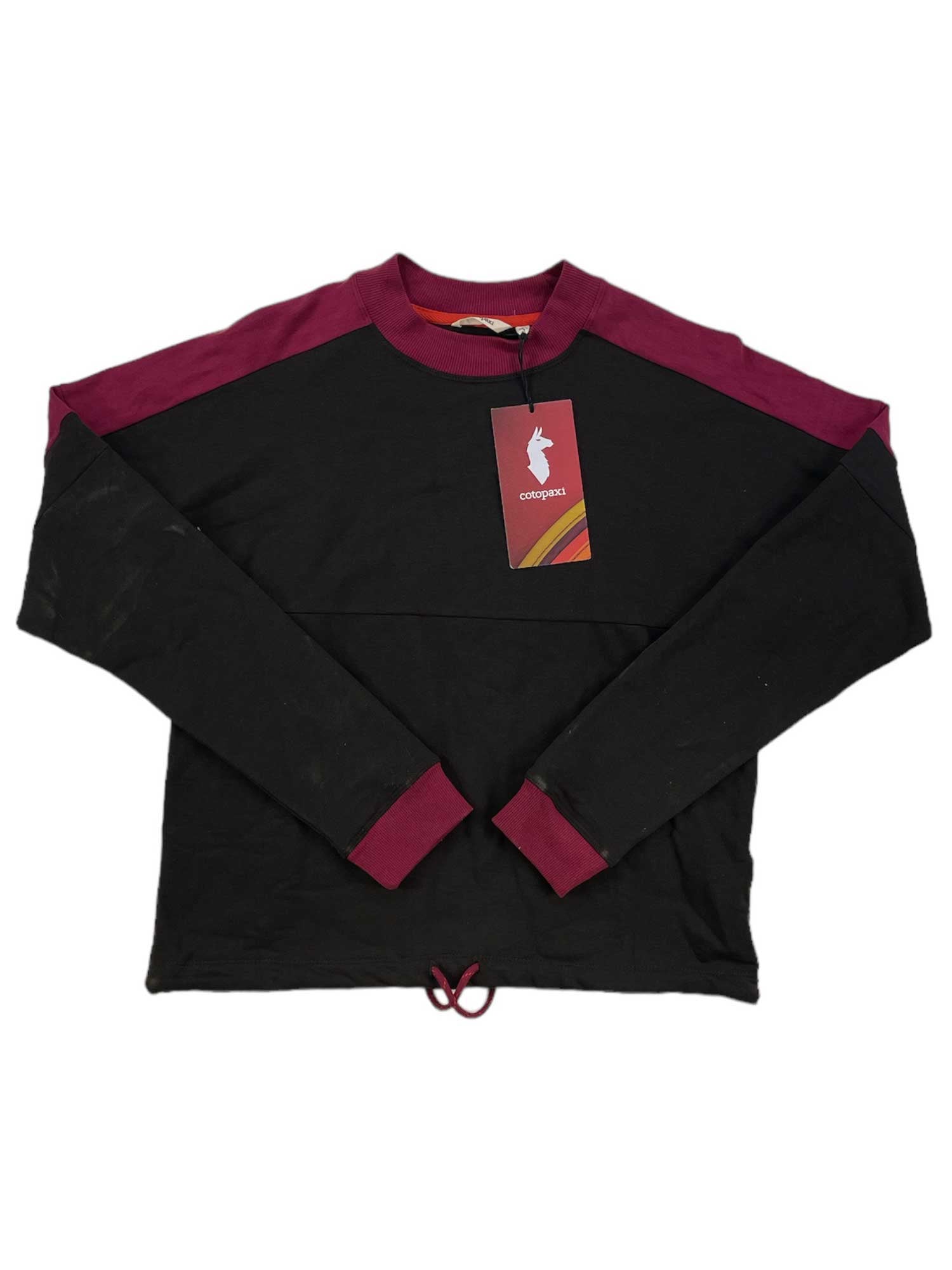 The Cotopaxi Womens Bandera Sweatshirt is a black long sleeve top with maroon cuffs, collar, and shoulder accents, made from moisture-wicking fabric. It is shown laid flat with a tag attached to the neckline.