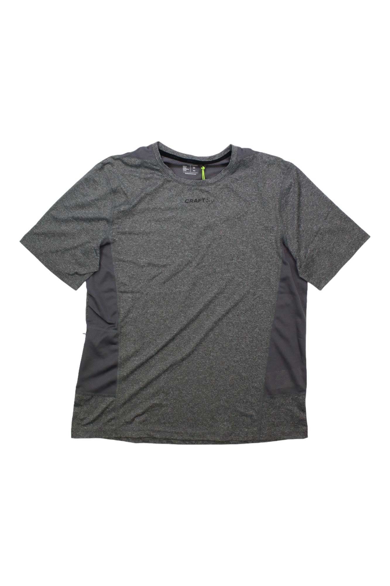 The Craft Sportswear Men's ADV Essence SS Tee is a dark gray moisture-wicking running shirt with light gray side panels, made from recycled polyester. It has a crew neckline and a small subtle logo on the chest, shown flat on a white background.