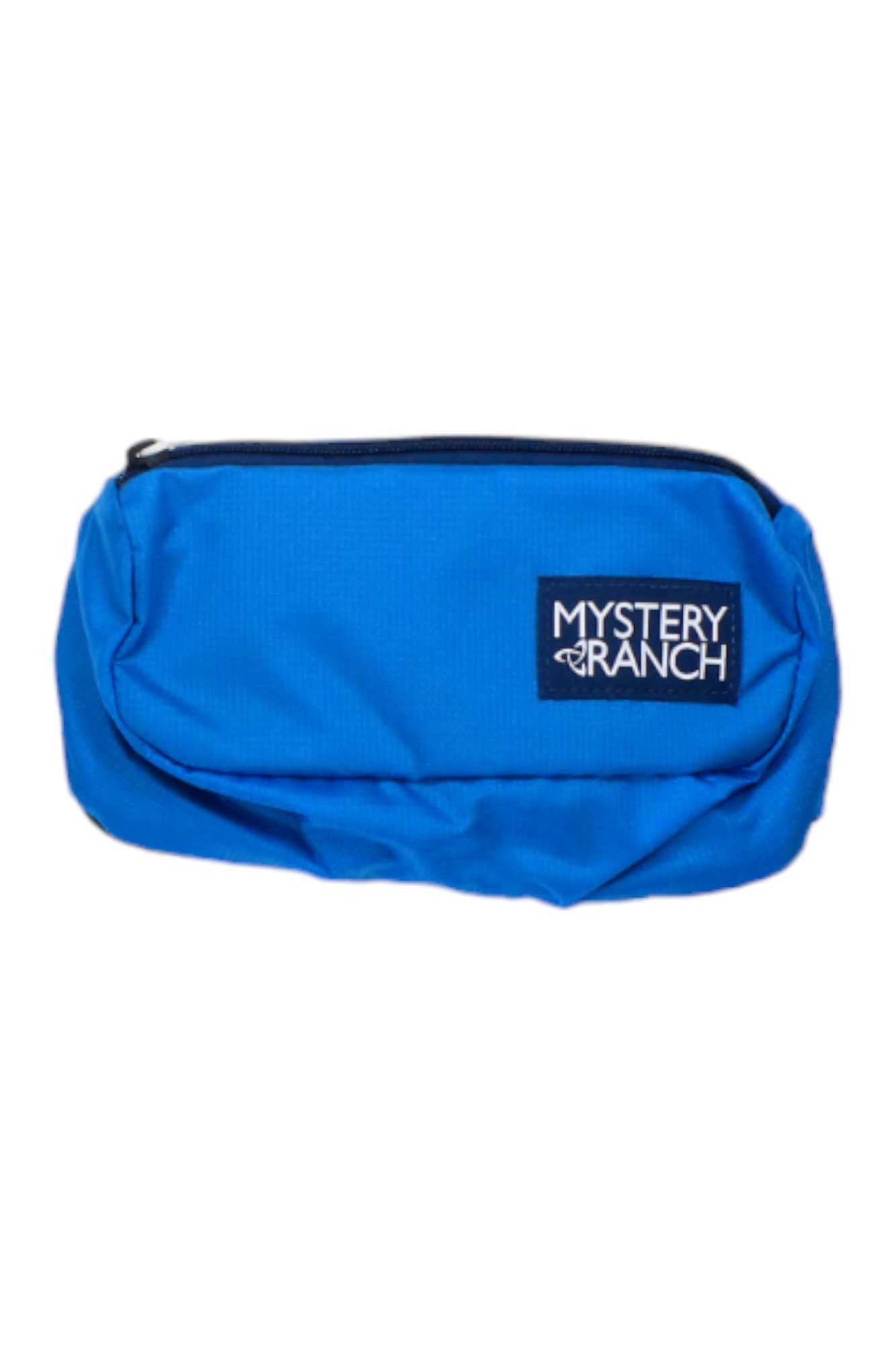 The Mystery Ranch Forager Hip Pack is a bright blue, zippered pouch with a black logo patch on the front. Its simple rectangular design and durable fabric make it perfect for outdoor adventures.