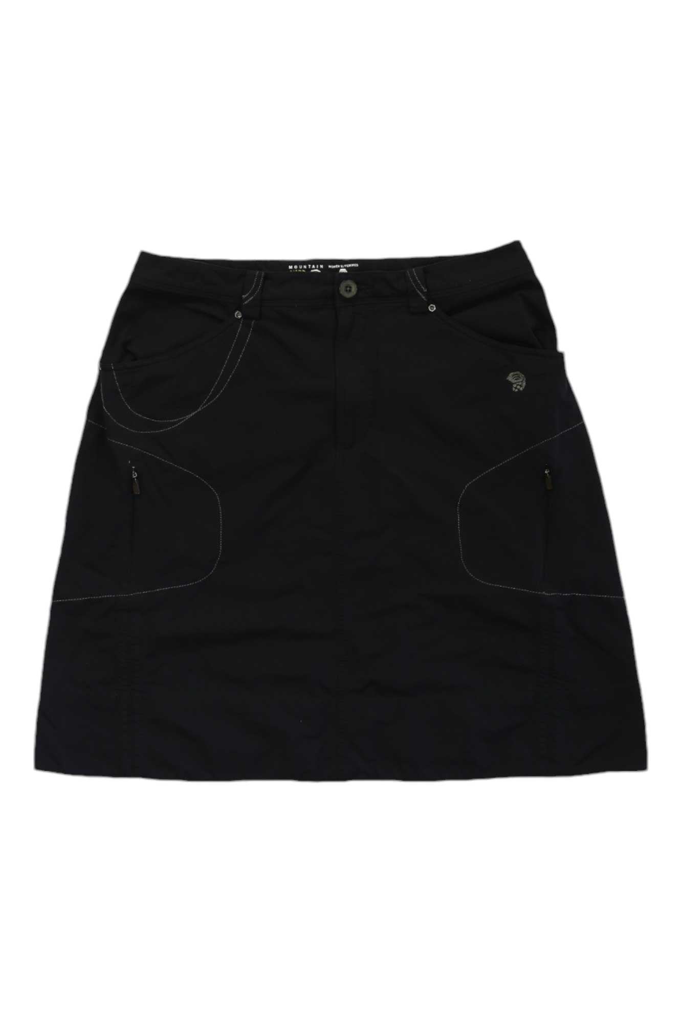 The Mountain Hardwear Women’s Active Knee Length Skirt is black, A-line, with front pockets, button and zipper closure, white stitching, and small zipper accents—ideal for everyday wear or outdoor adventures.