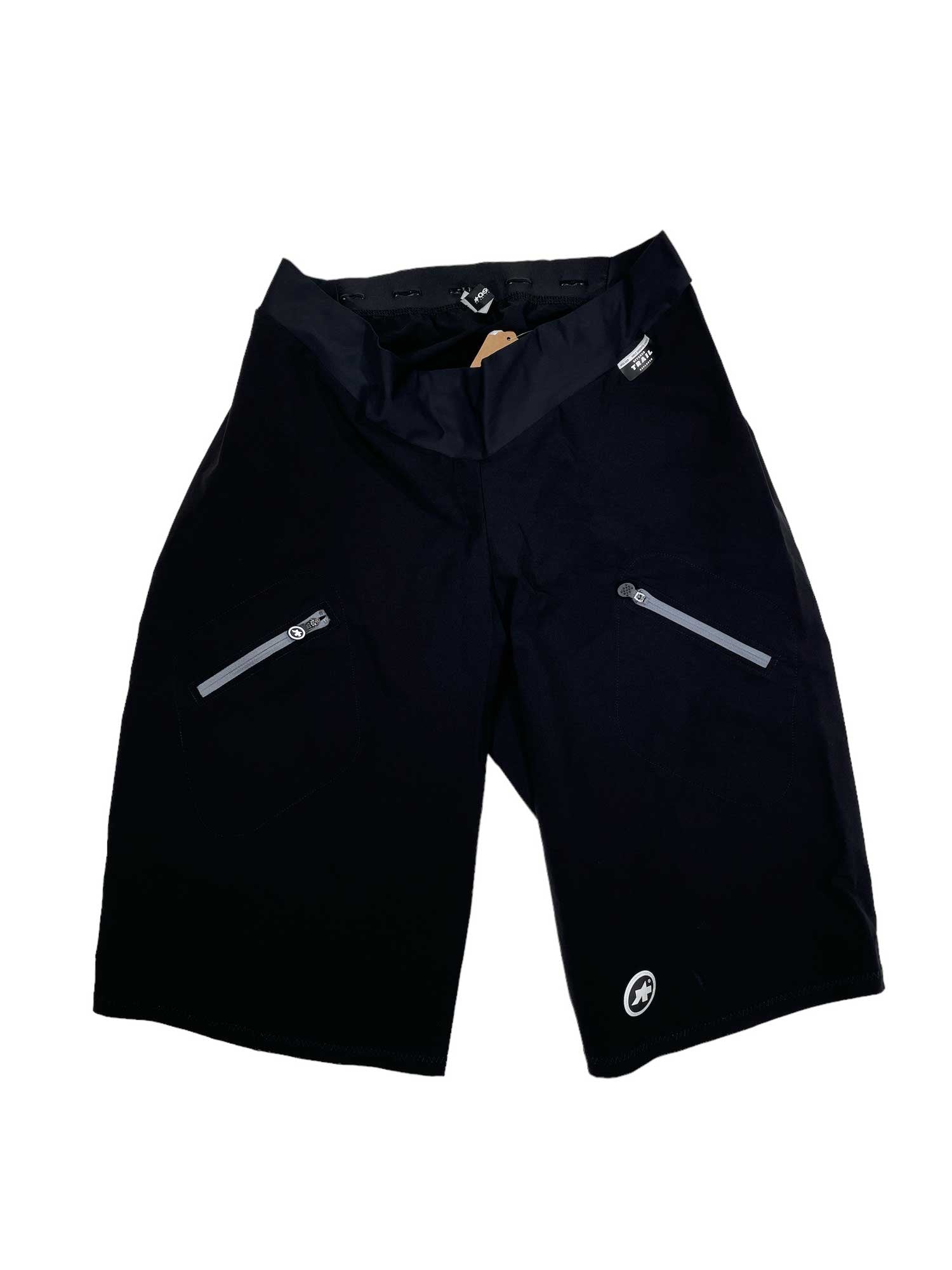 A pair of Assos Trail Winter Cargo Pants in black with zippered side pockets is laid flat on a white background. Made from ultralight textiles, these pants feature a small circular logo near the left hem.