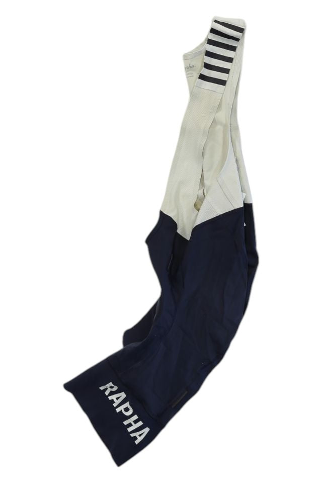 The Rapha Mens Pro Team Bib Shorts II - Regular feature navy blue legs, white upper straps with black horizontal stripes, RAPHA branding in white on one leg, and a race-grade chamois for superior comfort.