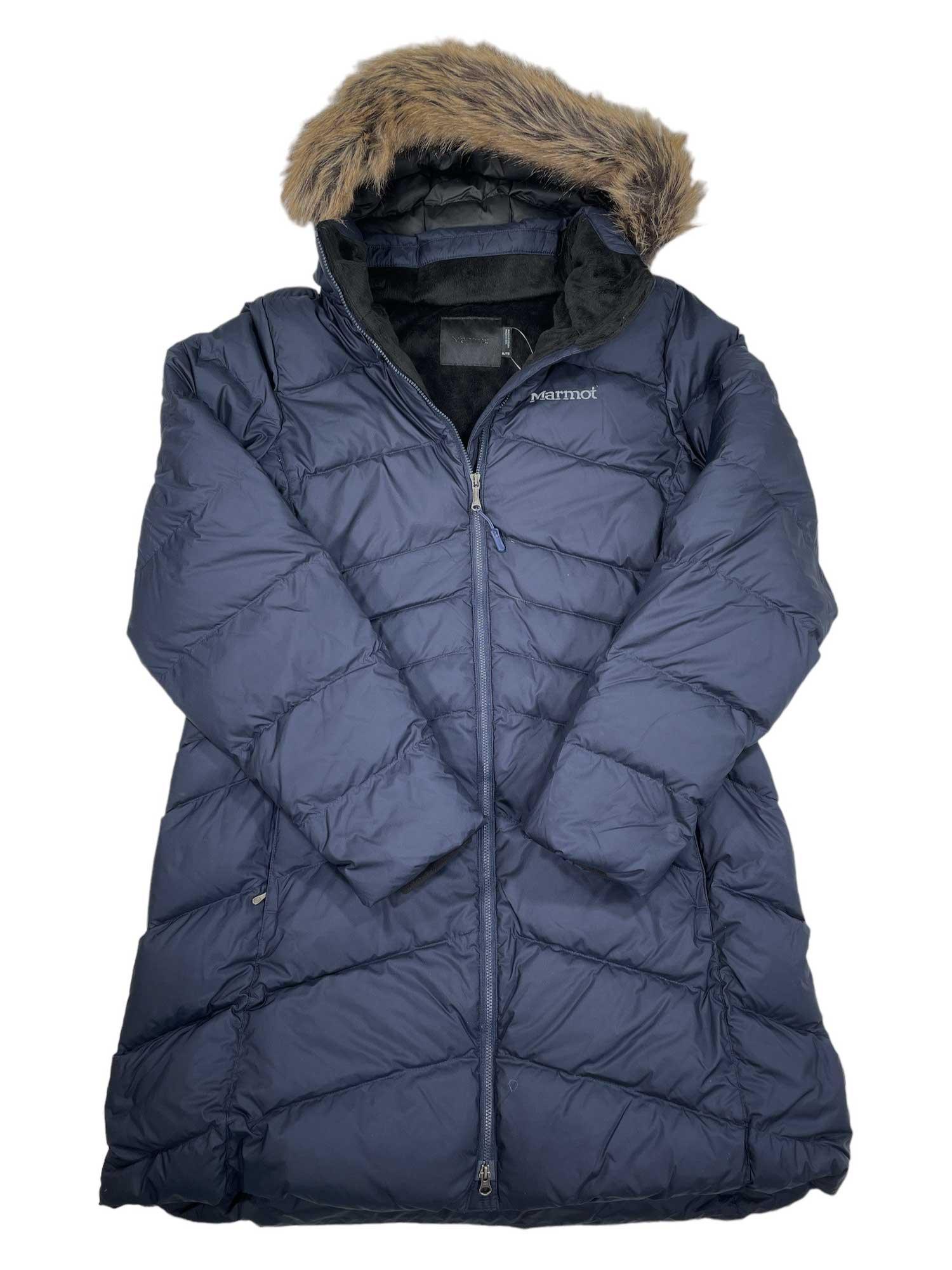 The Marmot Womens Montreal Down Coat is a navy blue, water-resistant, quilted winter coat with a faux fur-trimmed hood, front zipper, and Marmot logo on the chest. It’s displayed flat on a white background.