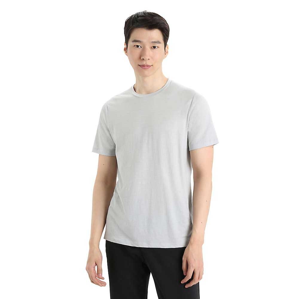 A person with short black hair wears the Icebreaker Mens Tech Lite II SS Tee in light gray and black pants, standing against a white background and facing the camera with a neutral expression.
