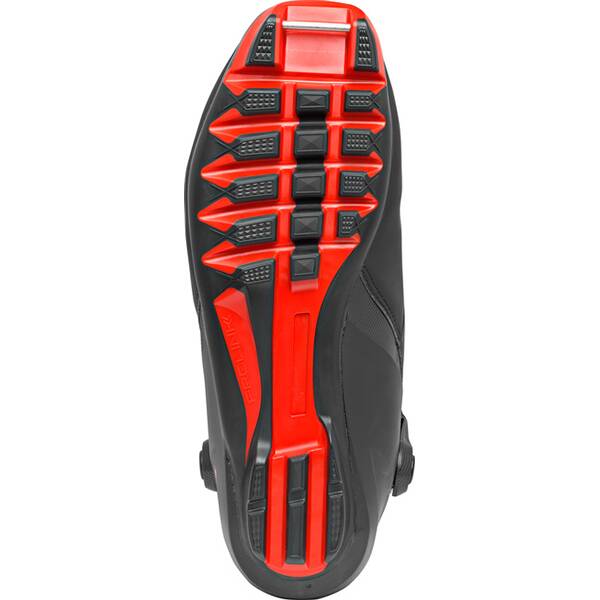 The image displays the sole of the Atomic Unisex Pro S2 Cross Country Ski Boots, featuring a black, textured design with horizontal red bars for enhanced traction and stability along the length, designed for an anatomical fit.