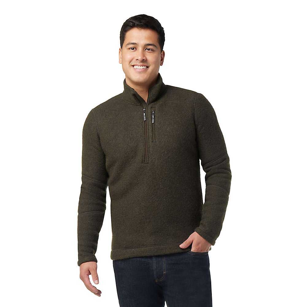 A man stands smiling against a white background, wearing blue jeans and a Smartwool Men's Hudson Trail Fleece Half Zip Sweater in dark green.