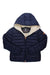 The Save The Duck Womens Gwen Jacket is navy blue with a front zipper, attached hood, light fleece lining, and orange logo patch on the left sleeve. This breathable jacket is water and wind resistant with a circular inner label logo.
