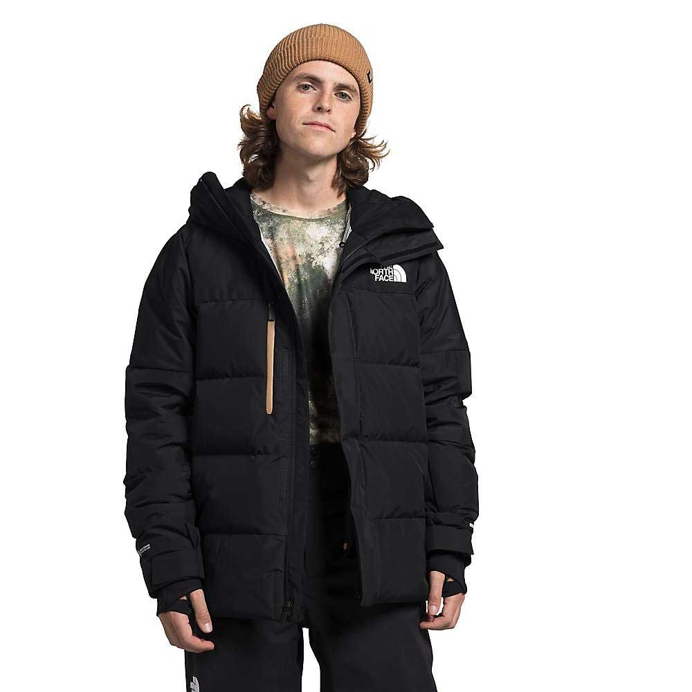 A person in a tan beanie, tie-dye shirt, and The North Face Mens Corefire Down Windstopper Jacket with logo stands against a white background, facing forward with a neutral expression.