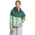 A woman wears The North Face Womens Antora Rain Hoodie in two-tone green with a zipper, adjustable hood and waist, paired with light gray pants, standing against a plain white background.