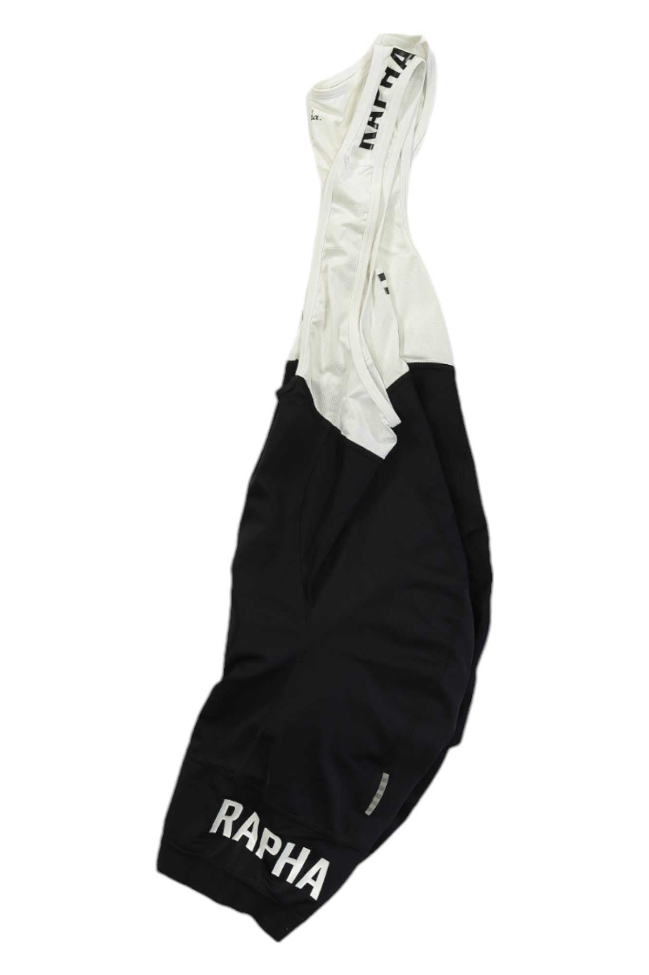 A pair of black and white Rapha Mens Pro Team Training Bib Shorts with ergonomic chamois and RAPHA branding on the left leg and shoulder strap, displayed flat on a white background.