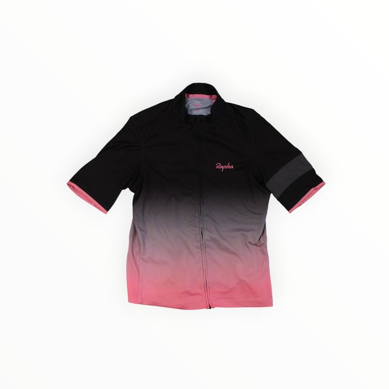 The Rapha Mens Super Lightweight Jersey is a short-sleeve cycling top with a black-to-pink gradient, front zipper, pink Rapha logo on the chest, and pink accents inside the sleeves and collar.