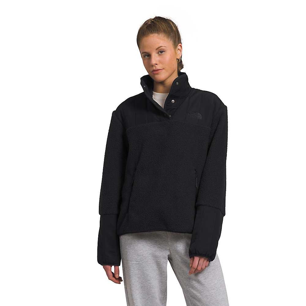 A person wears a black The North Face Women's Cragmont Fleece 1/4 Snap Top and light gray recycled polyester sweatpants, standing against a plain white background and looking at the camera with a neutral expression.