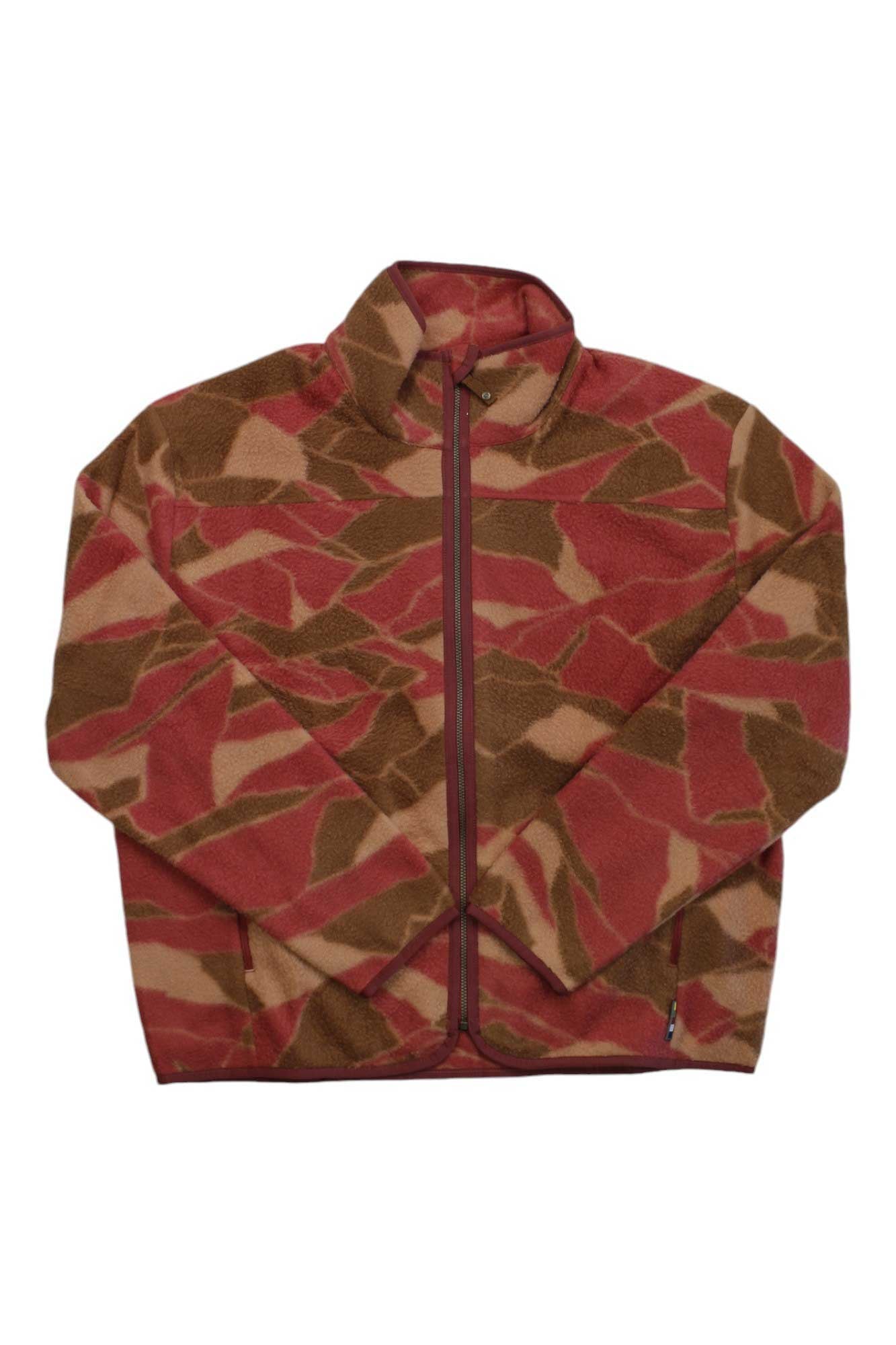 The Sherpa Womens Uddesya Eco Jacket is a zip-up fleece with a high collar, crafted from recycled polyester in brown, tan, and red camo. The women’s travel jacket is shown laid flat with sleeves crossed at the bottom.